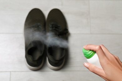Image of Woman spraying deodorant over pair of shoes at home, closeup