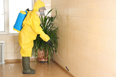 Photo of Pest control worker spraying pesticide on wall indoors. Space for text