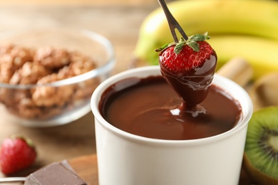 Photo of Dipping strawberry into fondue pot with chocolate, closeup