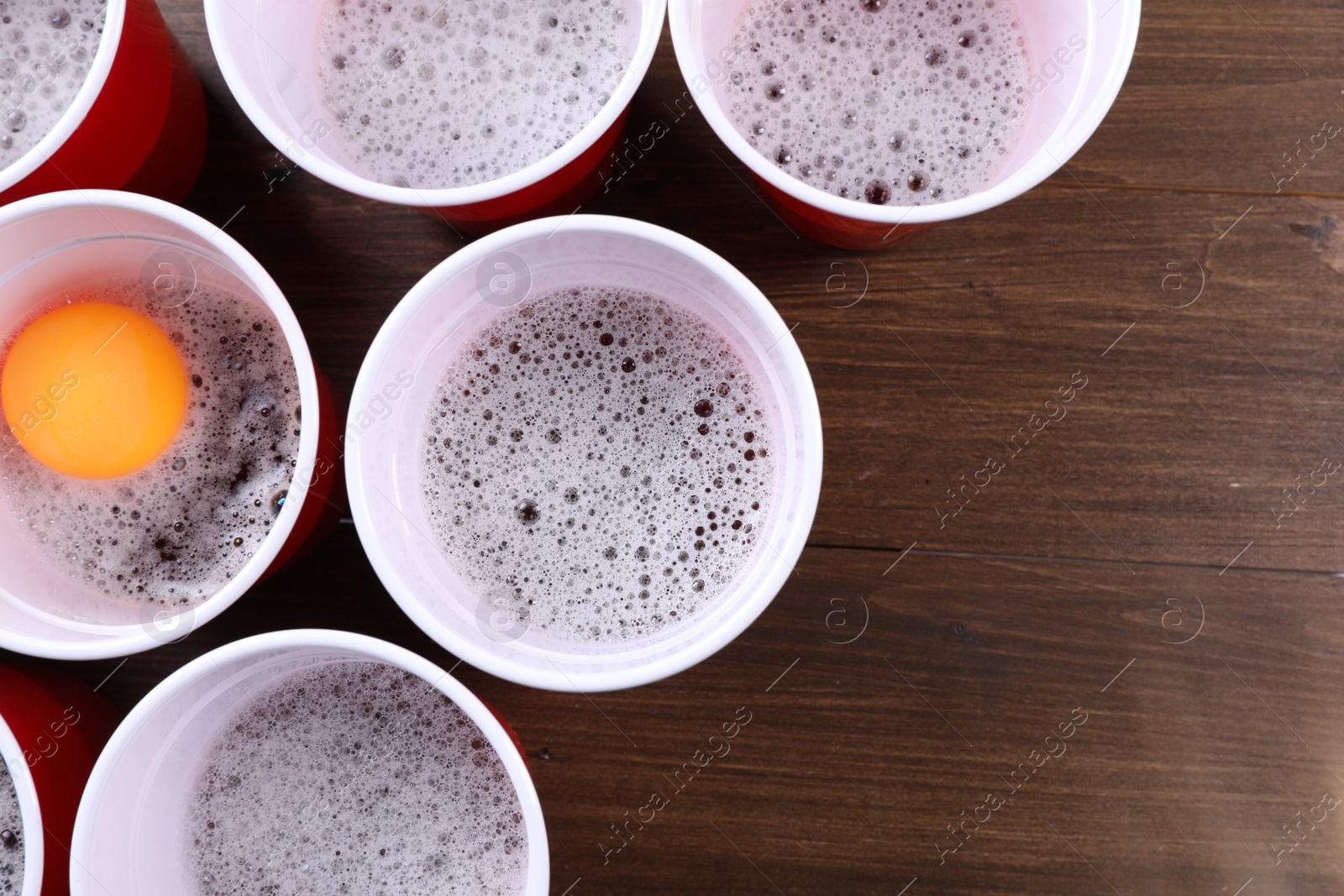 Photo of Plastic cups and ball on wooden table, flat lay with space for text. Beer pong game