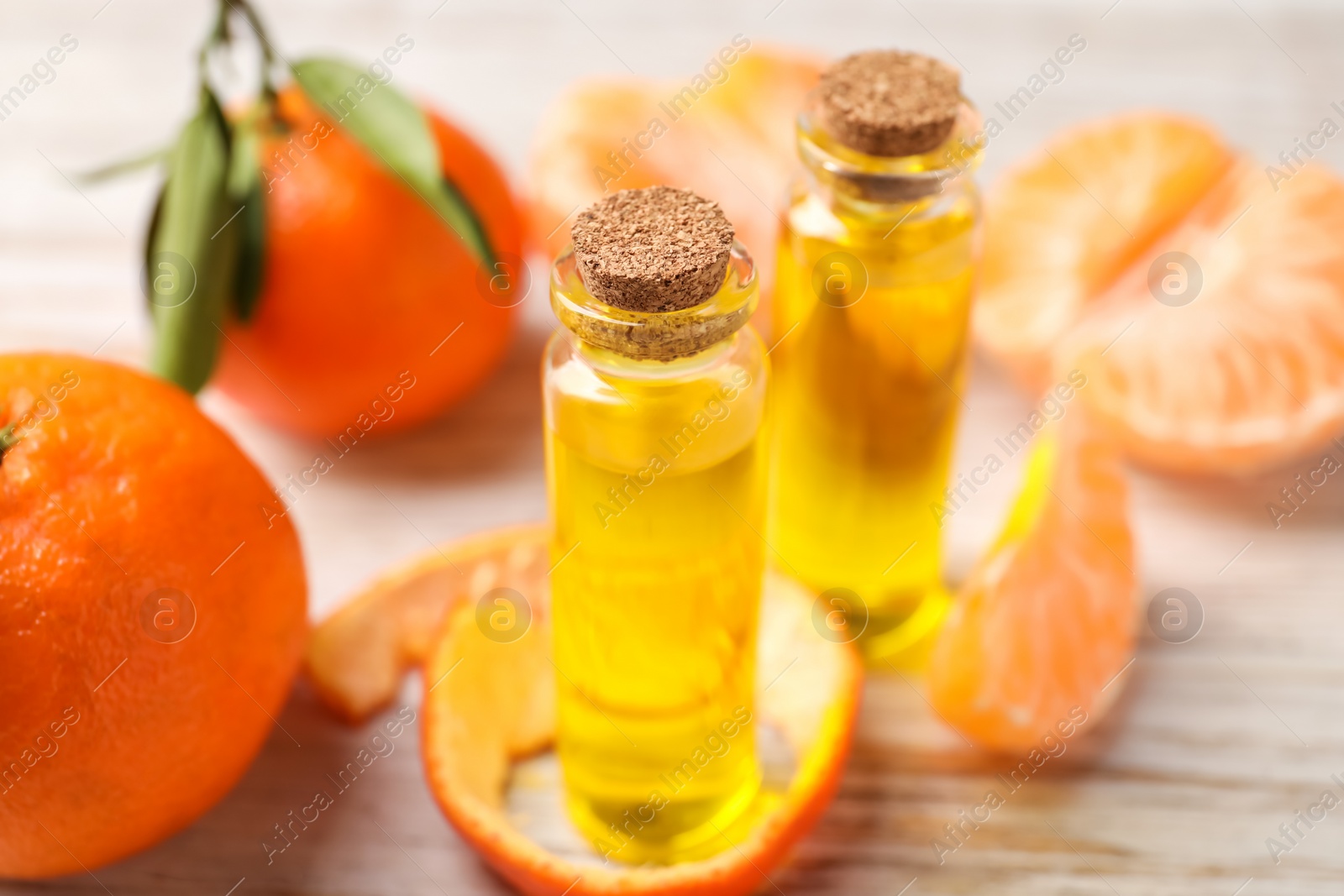 Photo of Bottles of tangerine essential oil, fresh fruits and peel on white wooden table, closeup