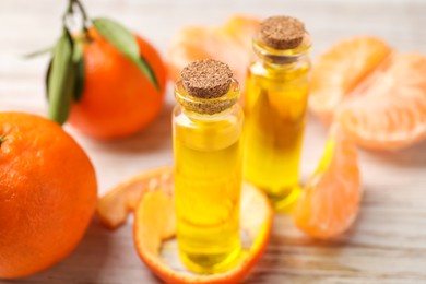 Bottles of tangerine essential oil, fresh fruits and peel on white wooden table, closeup