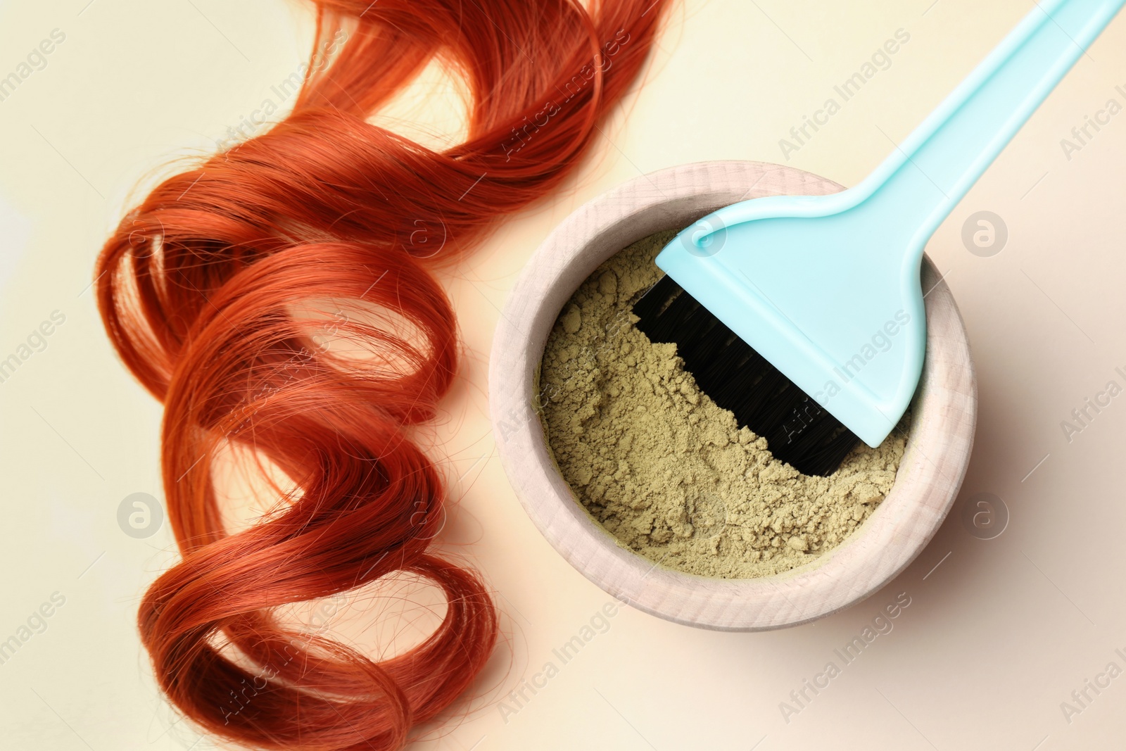 Photo of Bowl of henna powder, brush and red strand on beige background, flat lay. Natural hair coloring