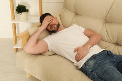Photo of Man suffering from pain in lower right abdomen on sofa at home. Acute appendicitis