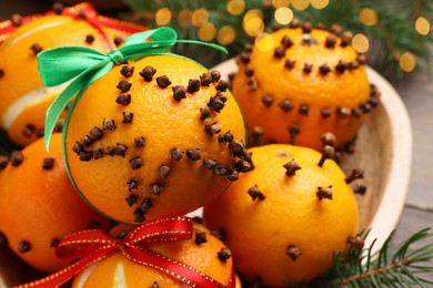 Pomander balls made of tangerines with cloves and fir branches on table, closeup
