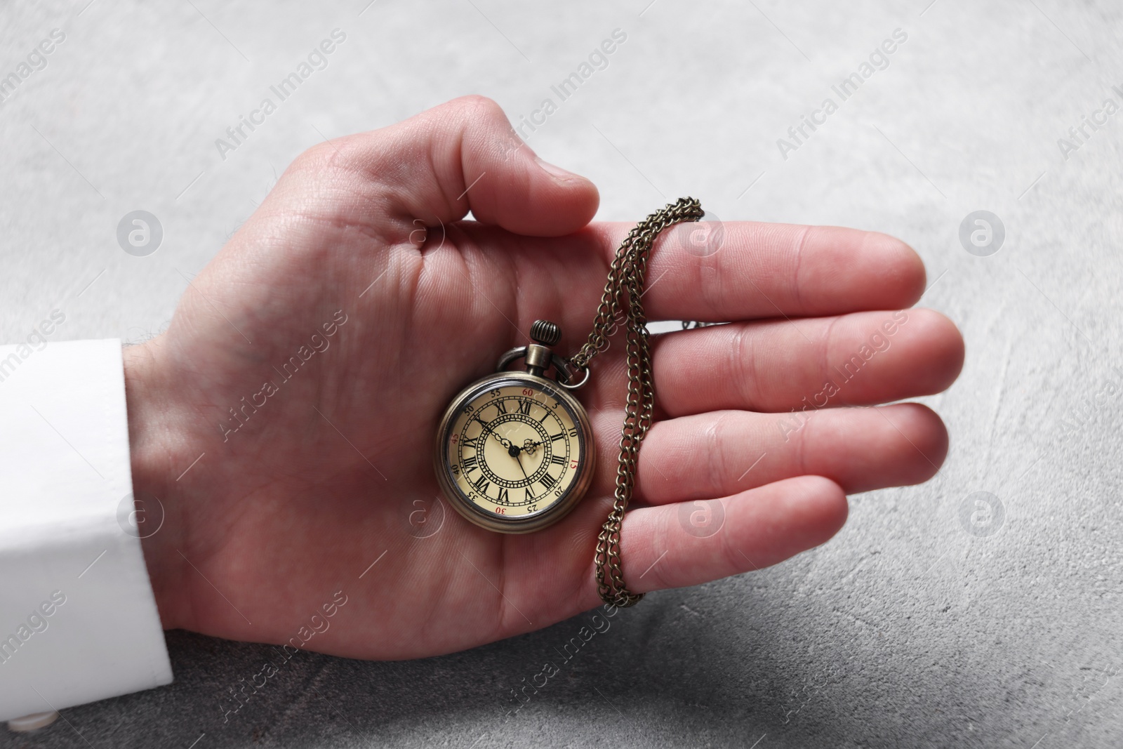 Photo of Man holding chain with elegant pocket watch at grey textured table, closeup