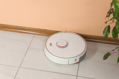 Photo of Robotic vacuum cleaner on white tiled floor near beige wall