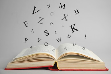 Image of Open book with letters flying out of it on light background