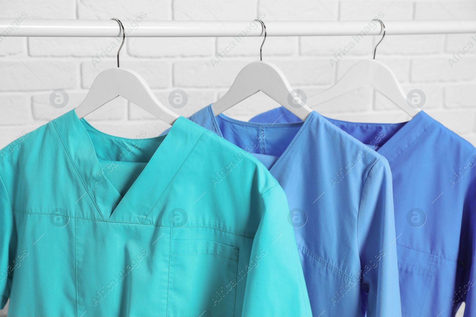 Photo of Medical uniforms hanging on rack near white brick wall, closeup