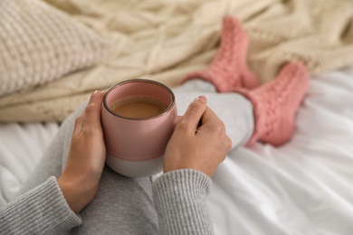 Woman with cup of hot coffee resting on bed, closeup
