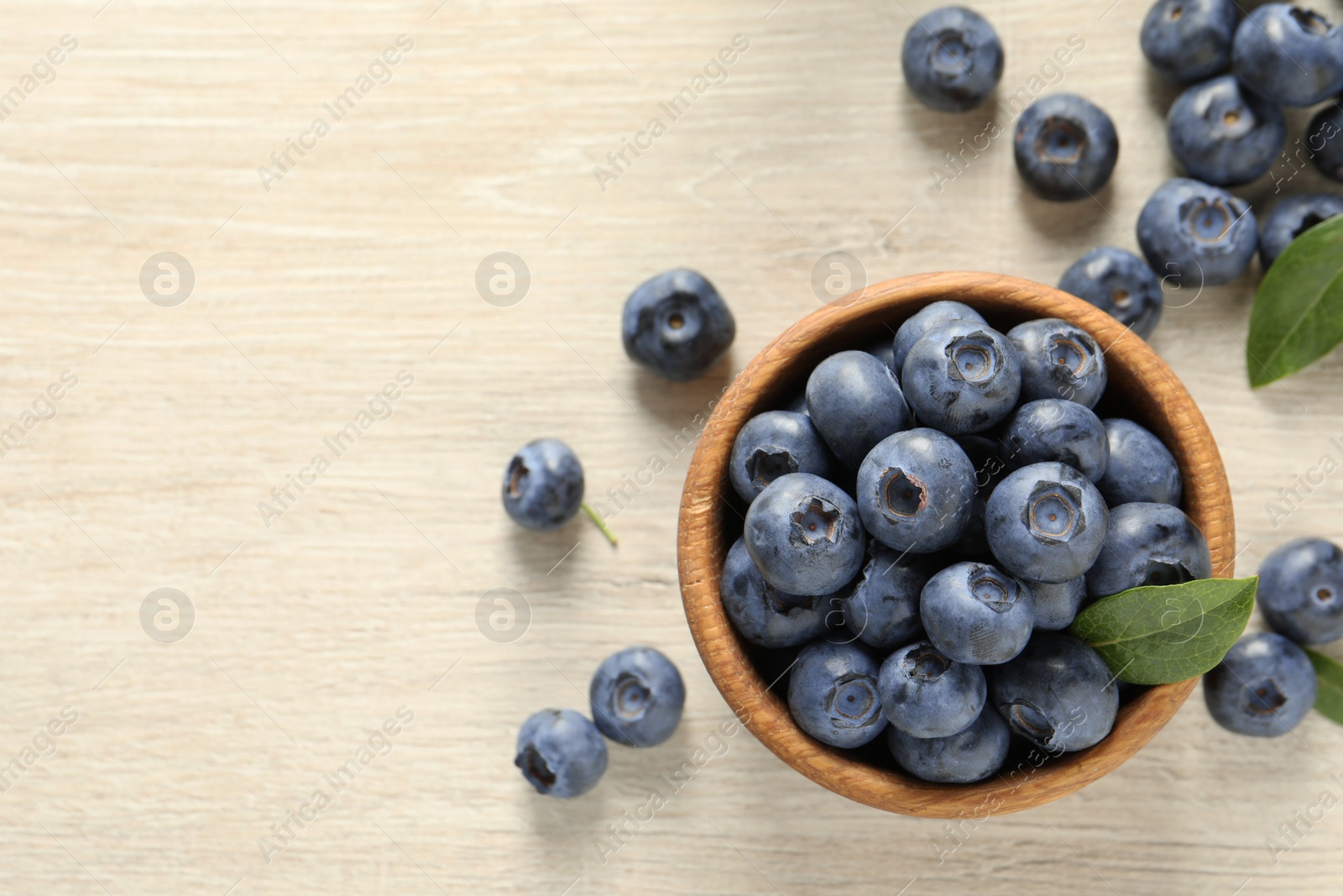 Photo of Bowl of fresh tasty blueberries on white wooden table, flat lay. Space for text