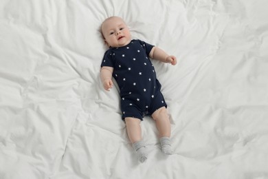 Photo of Cute baby lying on white bed, above view. Space for text