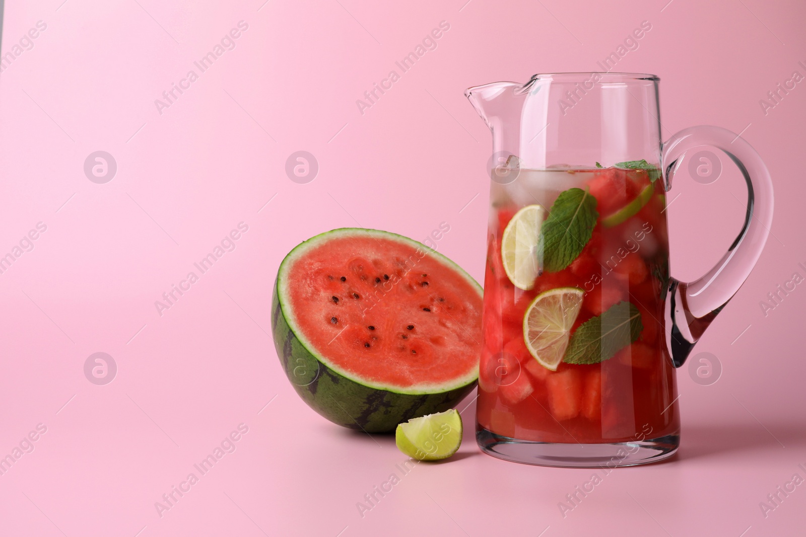 Photo of Tasty summer watermelon drink with lime in glass jug on pink background. Space for text