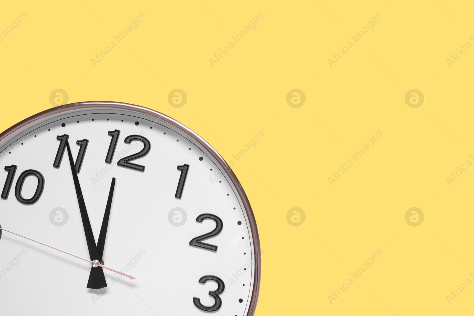 Photo of Clock showing five minutes until midnight on yellow background, top view with space for text. New Year countdown