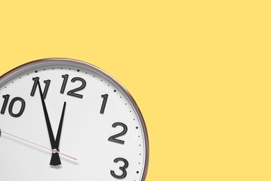 Clock showing five minutes until midnight on yellow background, top view with space for text. New Year countdown