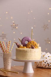Delicious cake decorated with sweets and burning candle on wooden table