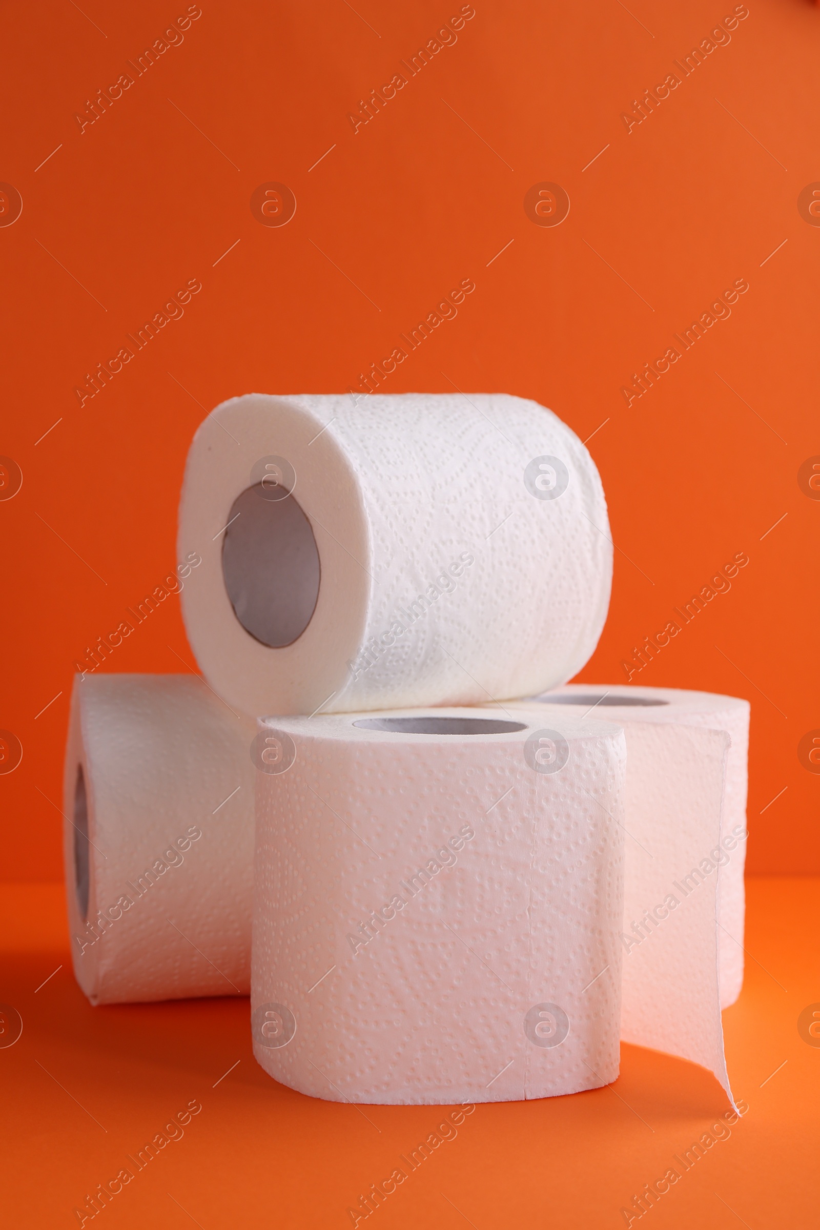 Photo of Soft toilet paper rolls on orange background, closeup