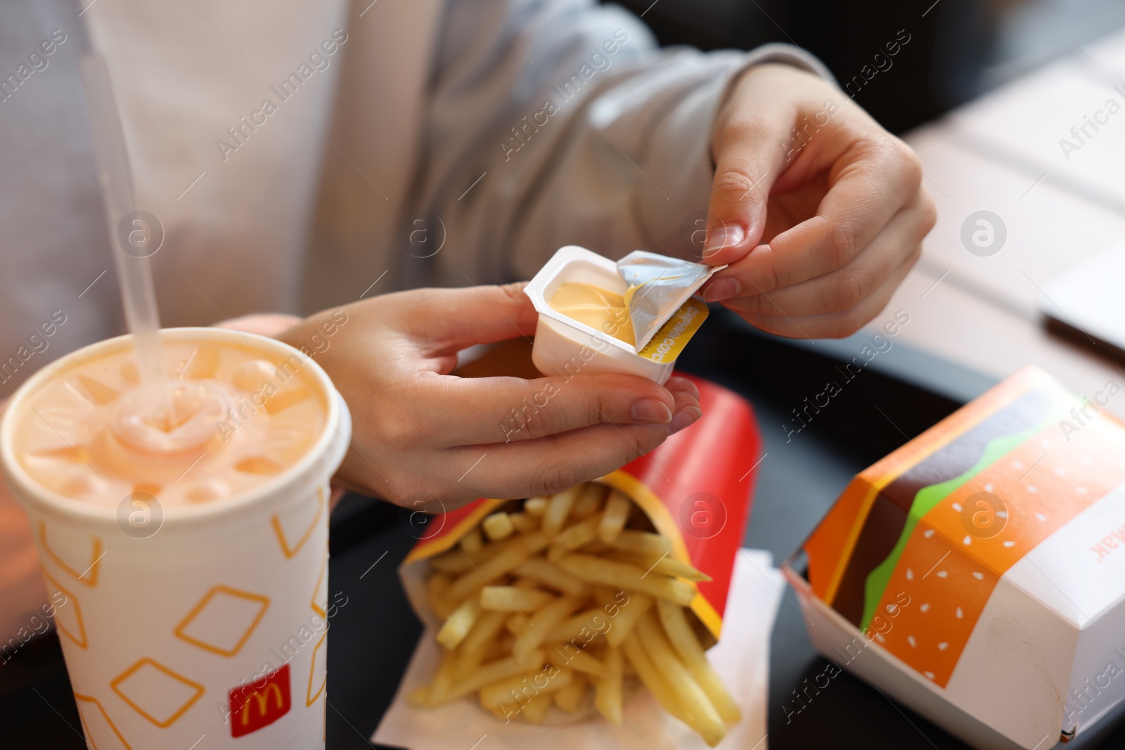 Photo of Lviv, Ukraine - September 26, 2023: Woman unpacking McDonald's sauce at table in restaurant, closeup