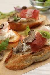 Photo of Delicious bruschettas with cheese, prosciutto and slices of black truffle on white wooden table, closeup