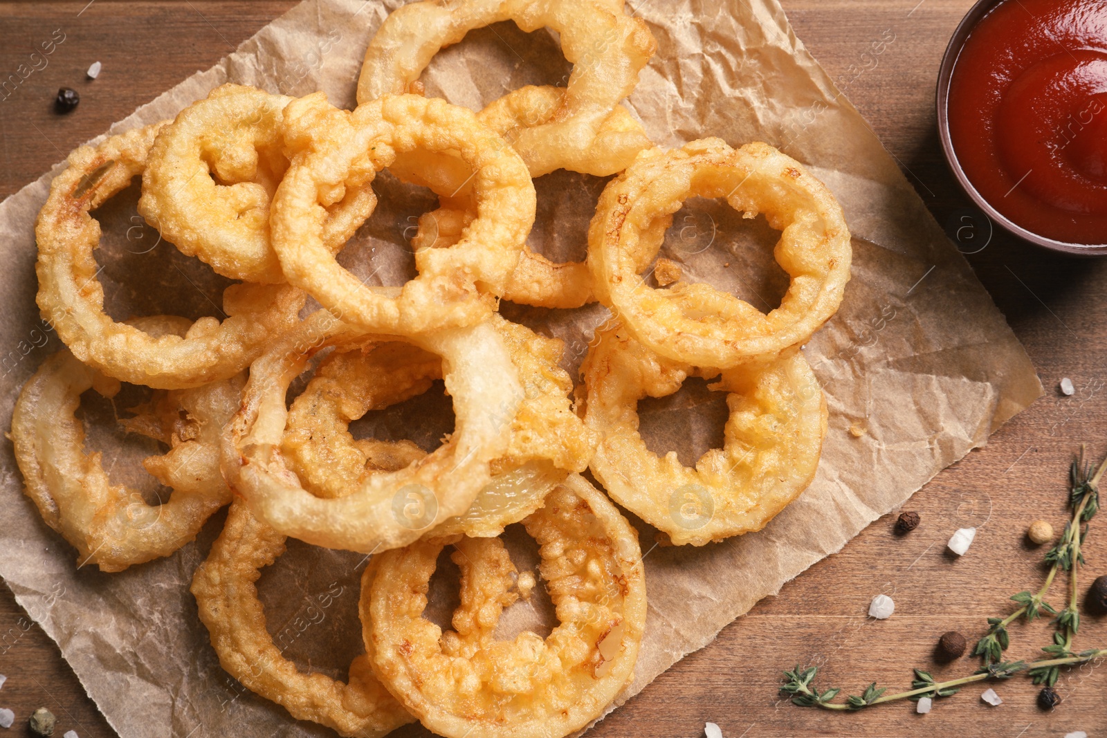 Photo of Homemade crunchy fried onion rings and sauce on wooden background, top view