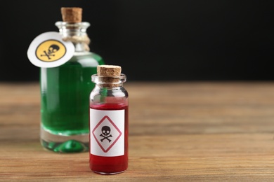 Photo of Glass bottle and vial of poison with warning signs on wooden table. Space for text