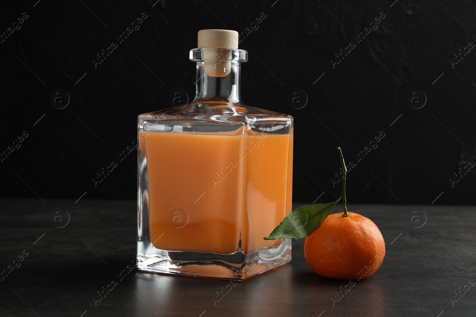 Photo of Delicious tangerine liqueur in glass bottle and fresh fruit on grey table