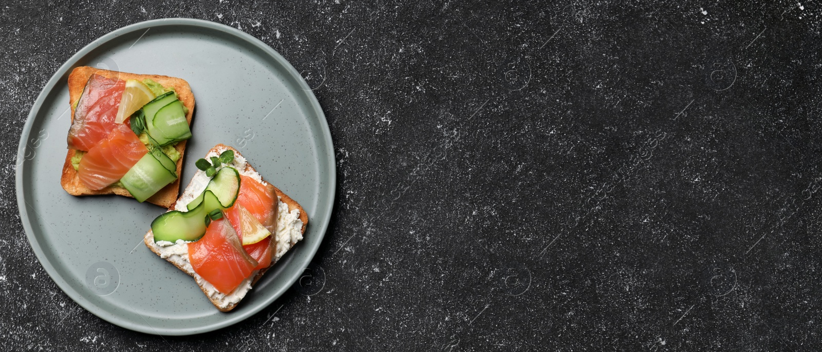 Image of Tasty toasts with salmon, cream cheese and cucumber on dark table, top view with space for text. Banner design