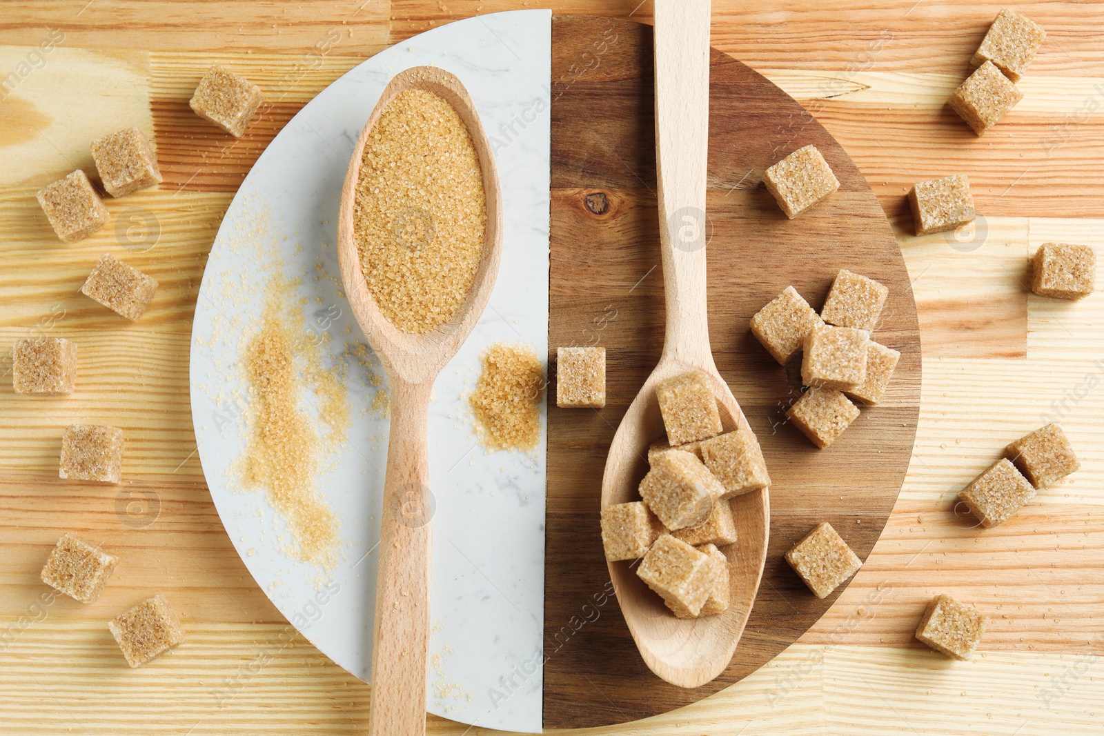 Photo of Brown sugar cubes and granulated in spoons on wooden table, flat lay