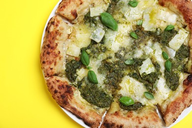 Photo of Delicious pizza with pesto, cheese and basil on yellow background, top view