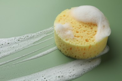 Yellow sponge with foam on green background, closeup