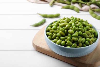 Bowl of delicious edamame beans on white wooden table, space for text