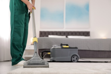 Photo of Professional janitor removing dirt from carpet with vacuum cleaner in bedroom, closeup. Space for text