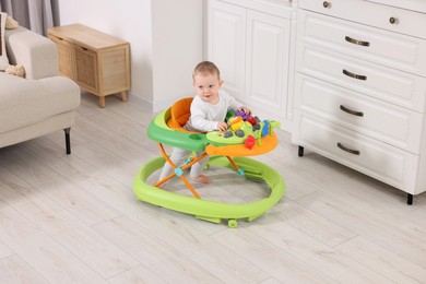 Photo of Cute little boy making first steps with baby walker at home
