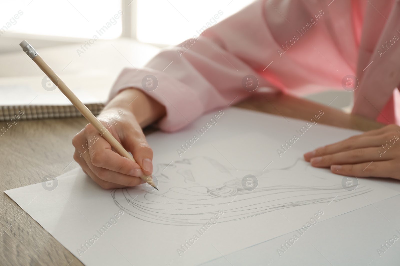 Photo of Woman drawing girl's portrait with pencil on sheet of paper at wooden table, closeup