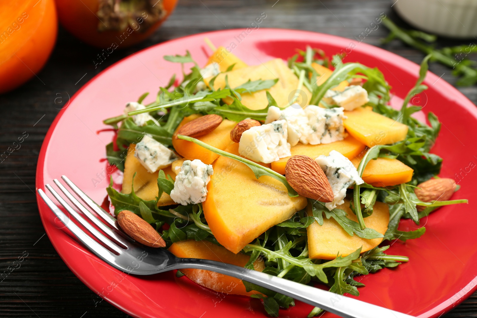 Photo of Delicious persimmon salad with blue cheese and arugula on table, closeup