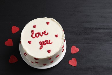 Photo of Bento cake with text Love You and paper hearts on black wooden table, space for text. St. Valentine's day surprise