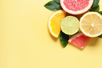 Different cut citrus fruits and leaves on yellow table, flat lay. Space for text