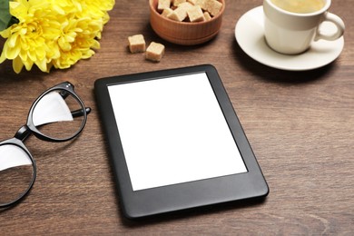 Photo of E-book reader, cup of coffee and glasses on wooden table. Space for text