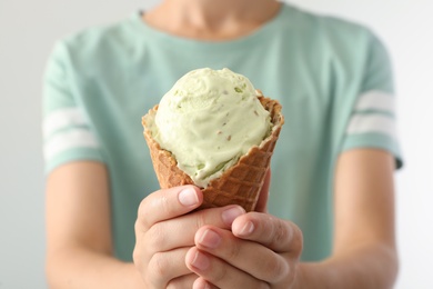 Photo of Woman holding green ice cream in wafer cone on light background, closeup