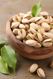 Delicious pistachios in bowl on wooden table, closeup