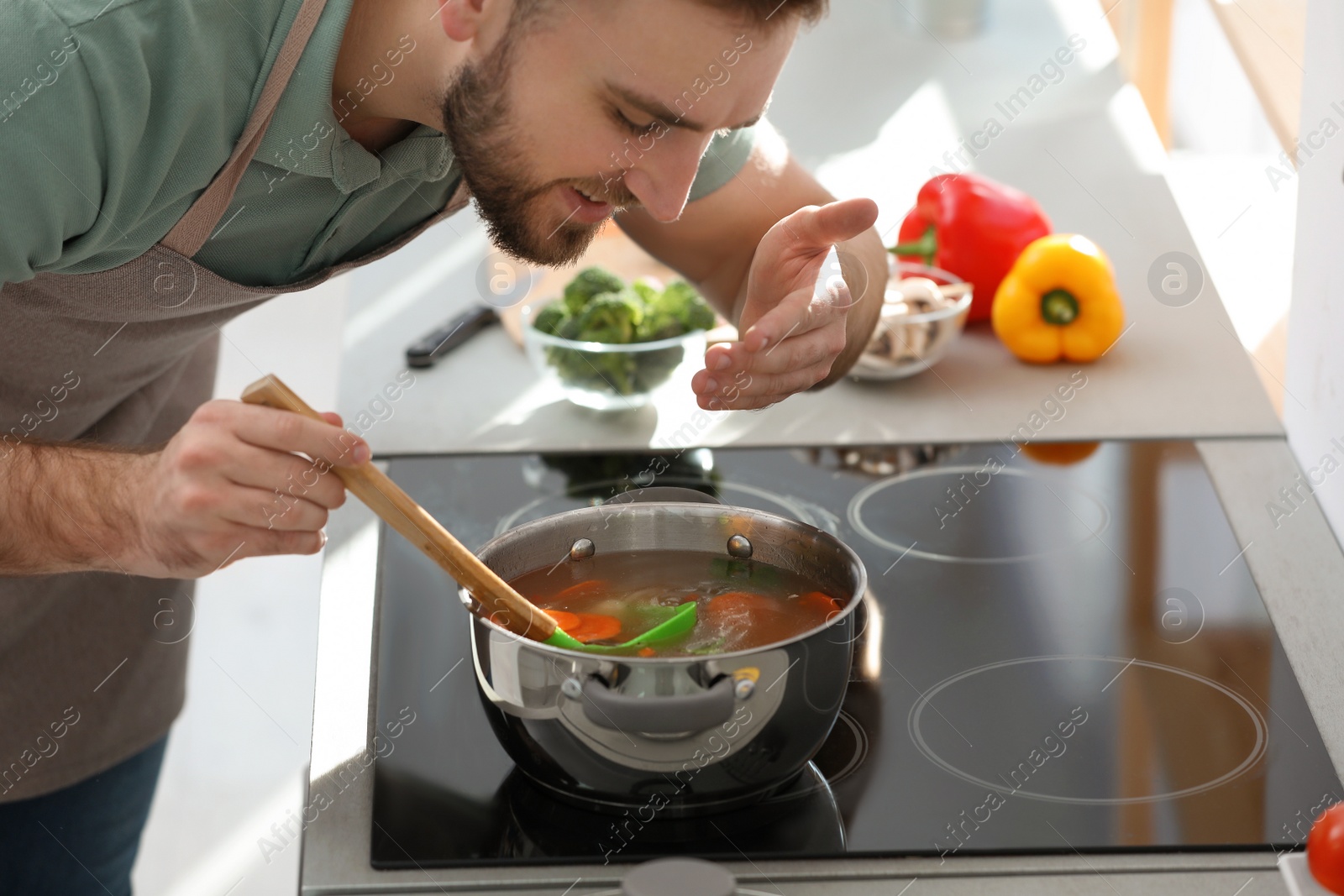 Photo of Young man cooking delicious soup in kitchen