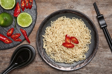 Plate of tasty noodles and chopsticks served on wooden table, flat lay