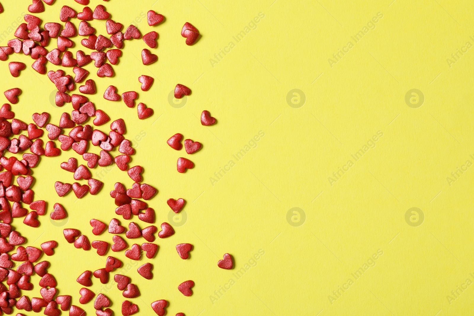 Photo of Bright heart shaped sprinkles on yellow background, flat lay. Space for text