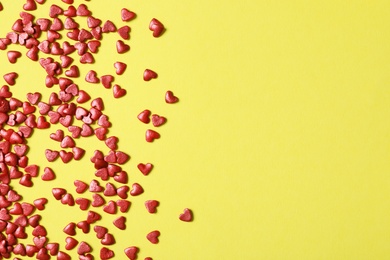 Bright heart shaped sprinkles on yellow background, flat lay. Space for text