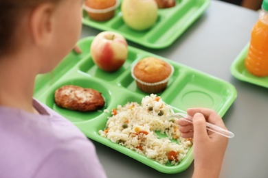 Photo of Girl sitting at table and eating healthy food during break at school, closeup
