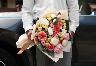 Photo of Young man with beautiful flower bouquet near car outdoors, closeup view