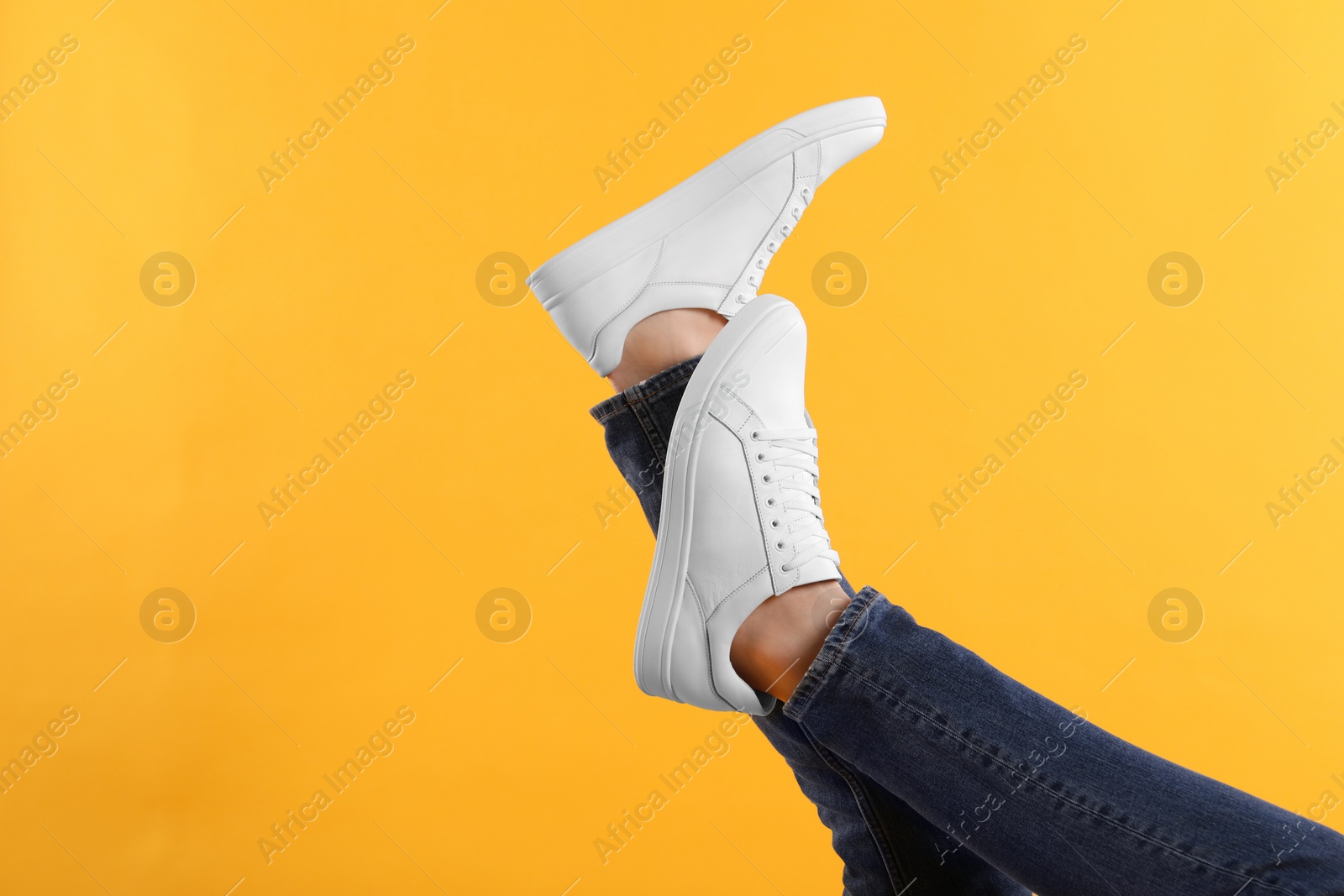 Photo of Man wearing stylish white sneakers on yellow background, closeup