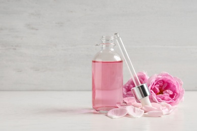 Photo of Fresh flowers, bottle of rose essential oil and pipette on table, space for text