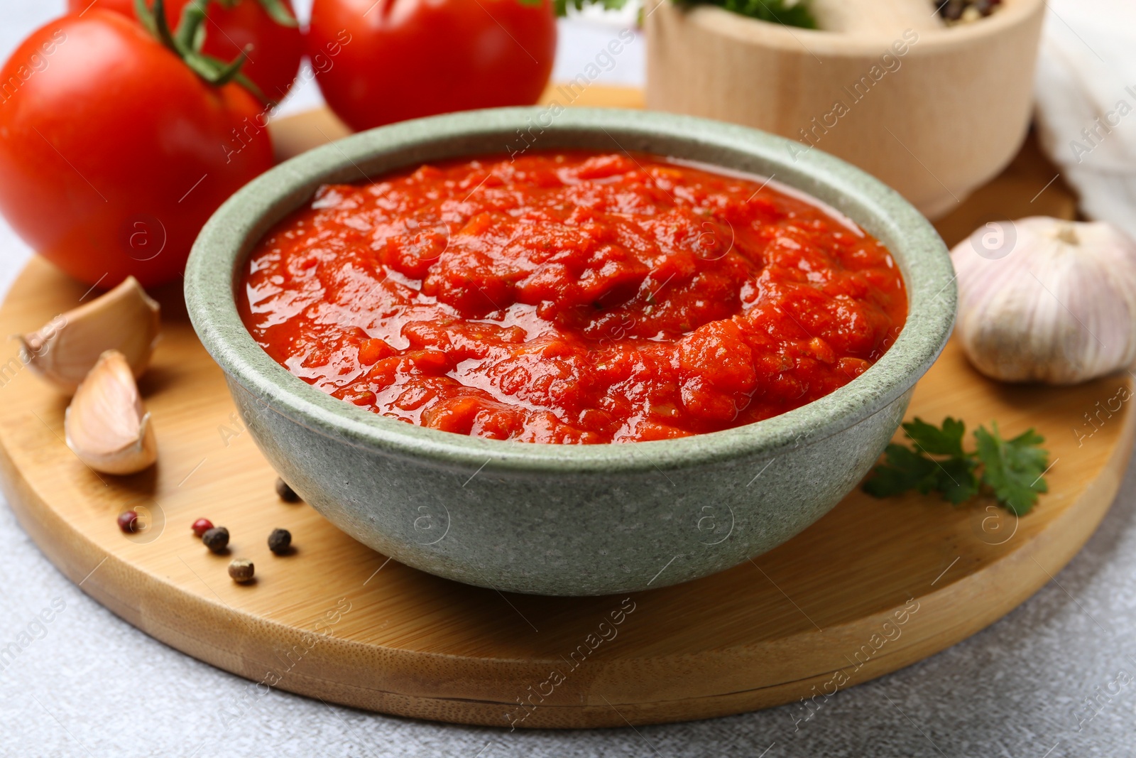 Photo of Homemade tomato sauce in bowl and fresh ingredients on light grey table, closeup