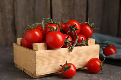 Many ripe red tomatoes in wooden crate on grey table